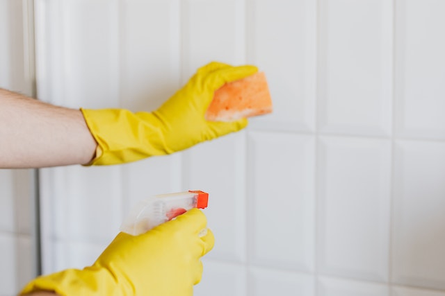person in yellow cleaning gloves holding orange sponge